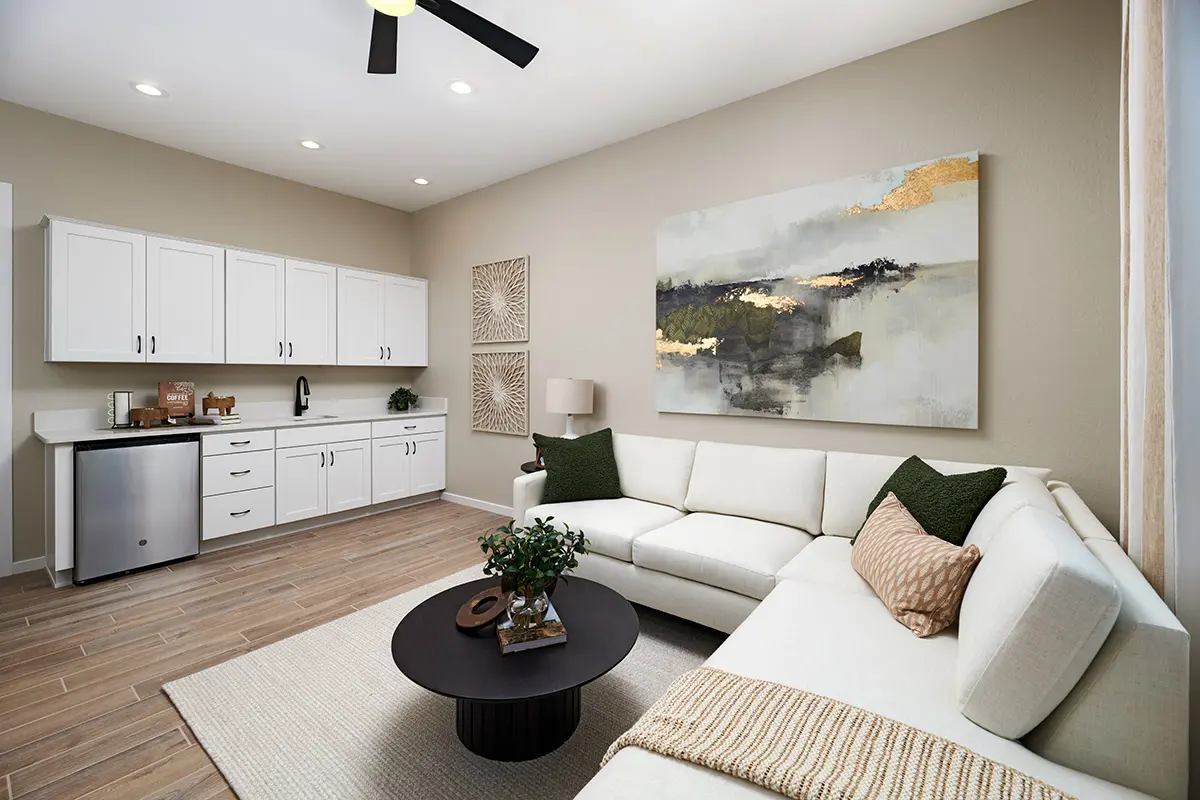 A living room with a sectional sofa, coffee table, and a kitchenette along the wall